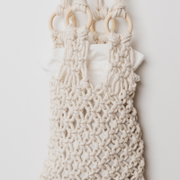 Cream macrame shoulder bag with a textured openwork pattern, wooden ring handles, and a white ruffled fabric insert, shown against a plain off-white background.